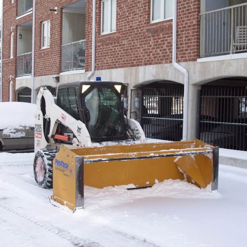 A ProTech Snow Pusher removing snow from the parking lot of an apartment complex.