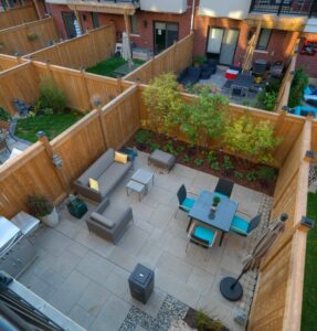 Cozy courtyard with patio furniture, greenery, and wooden fencing. Adjacent patios visible. Brick building backdrop. Peaceful outdoor setting for relaxation and gatherings.